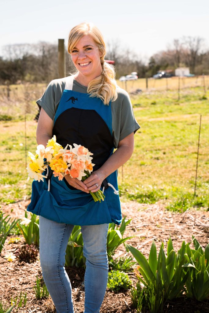Woman wearing a blue Roo Garden Apron holding daffodils.